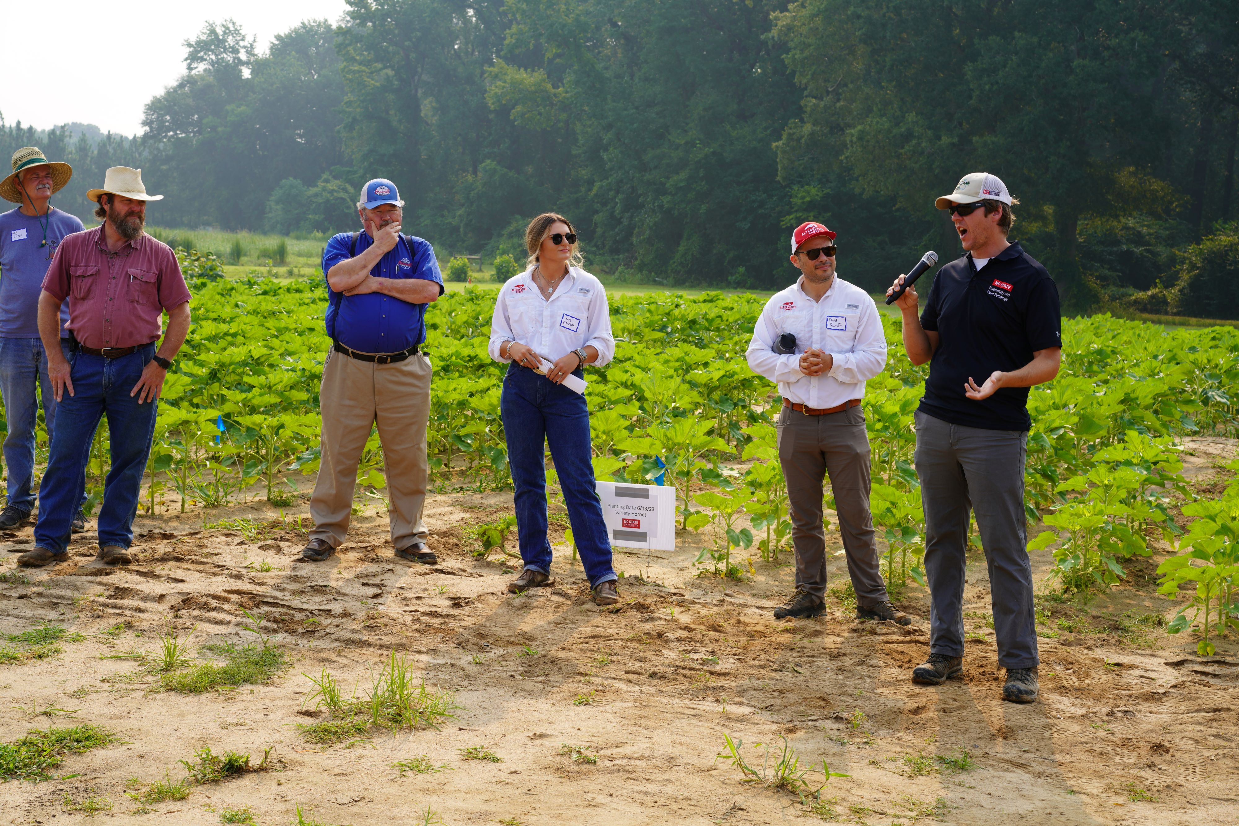 A man gives a talk to a group of farmers in a field.